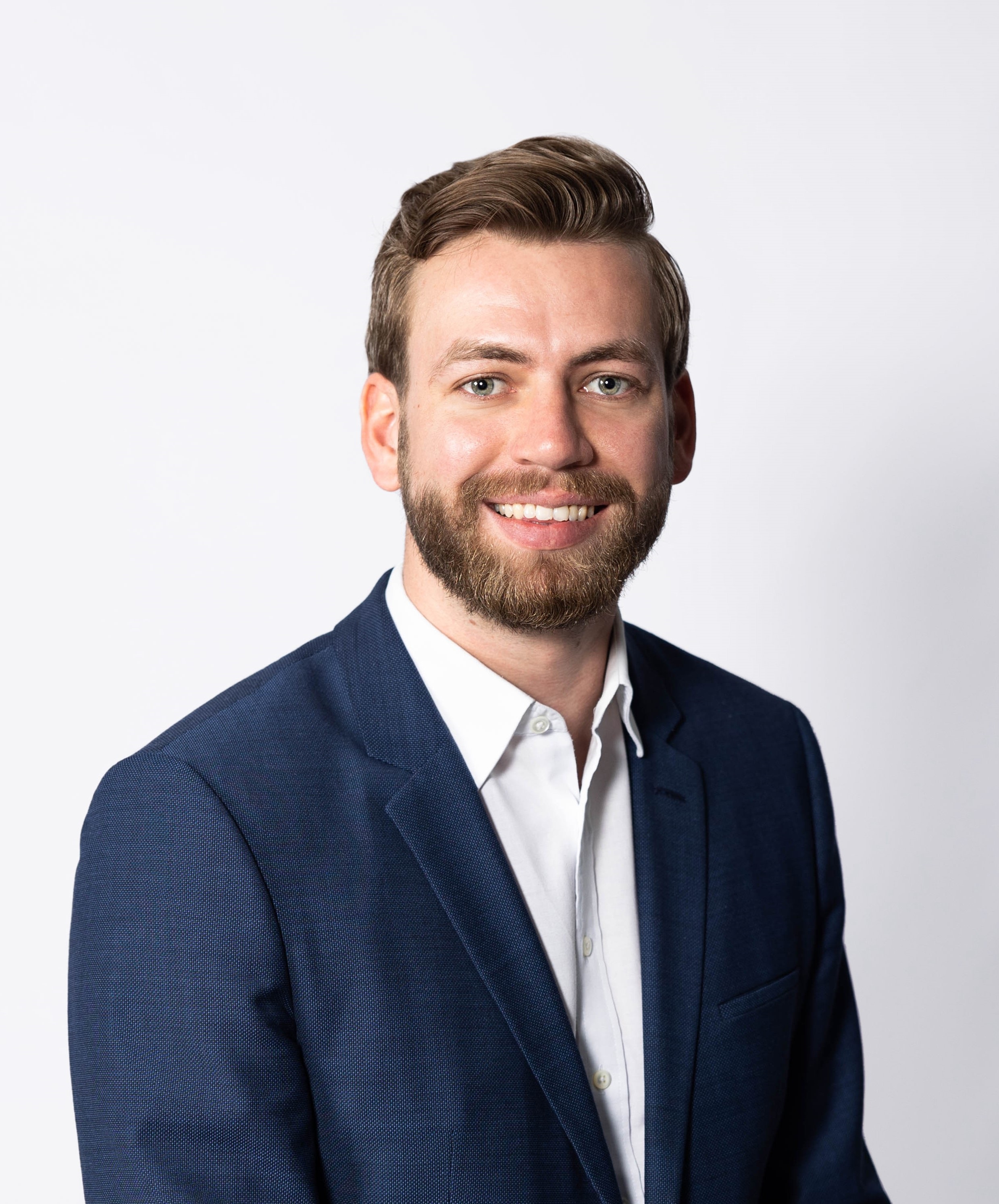 Portrait of a man with a friendly expression, wearing a dark blue suit and white shirt, against a plain white background.